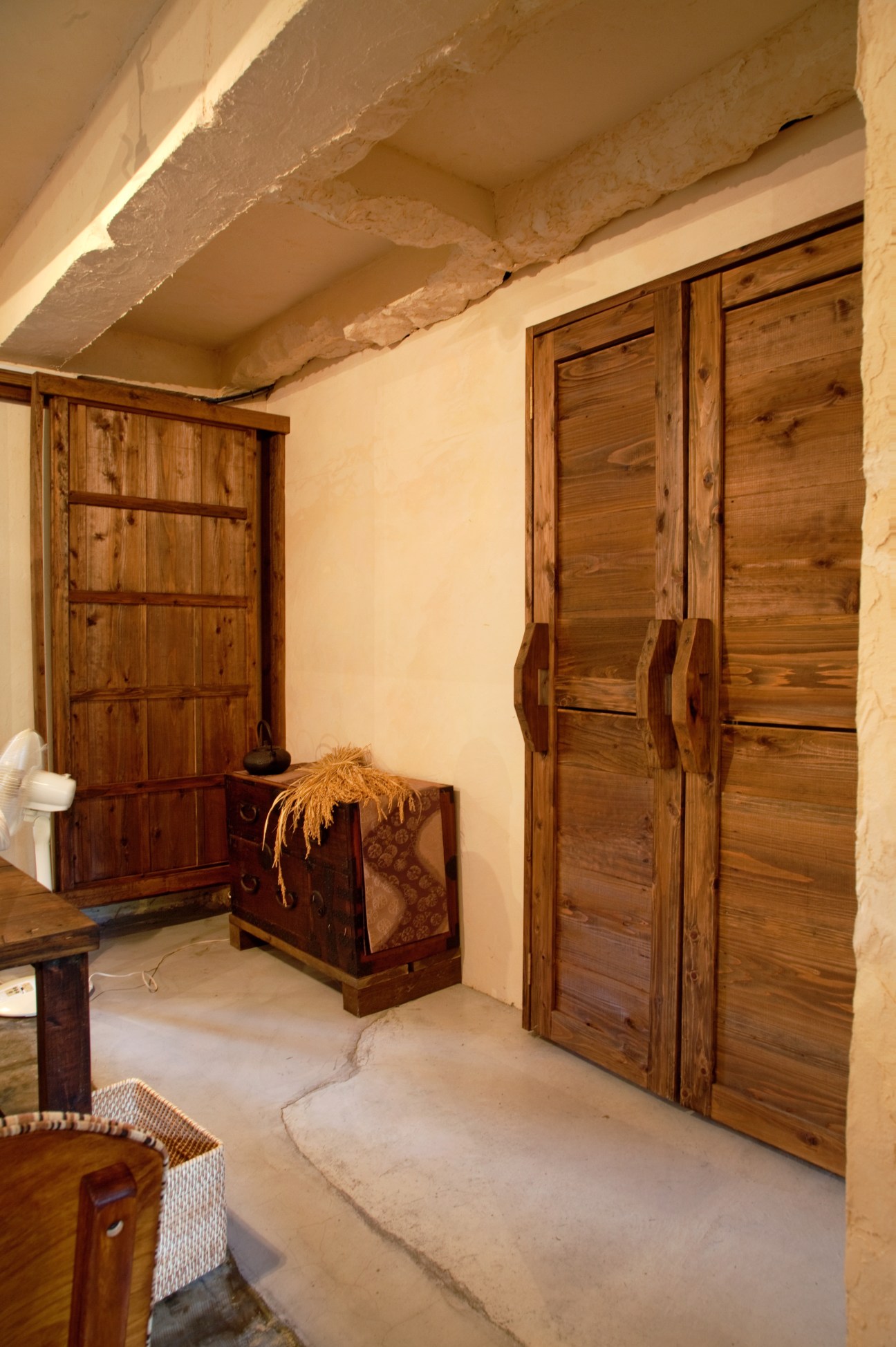 Interior of a concrete storage room with wooden cabinet doors and vintage furniture in Komeya Matsukura's rice storage space.