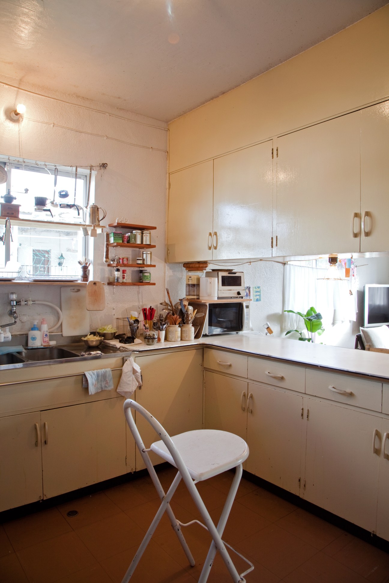 Kitchen with cream-colored cabinets, vintage appliances, and wooden shelving in a post-war military house.