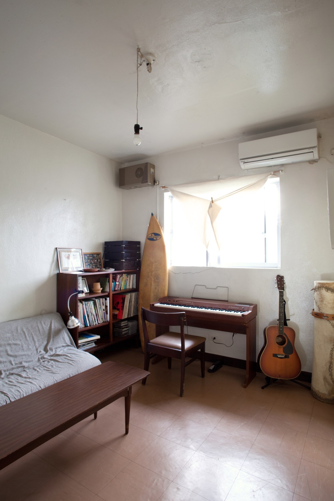 A spacious guest room with musical instruments, including a keyboard and acoustic guitar, shelving with books, and a bed.