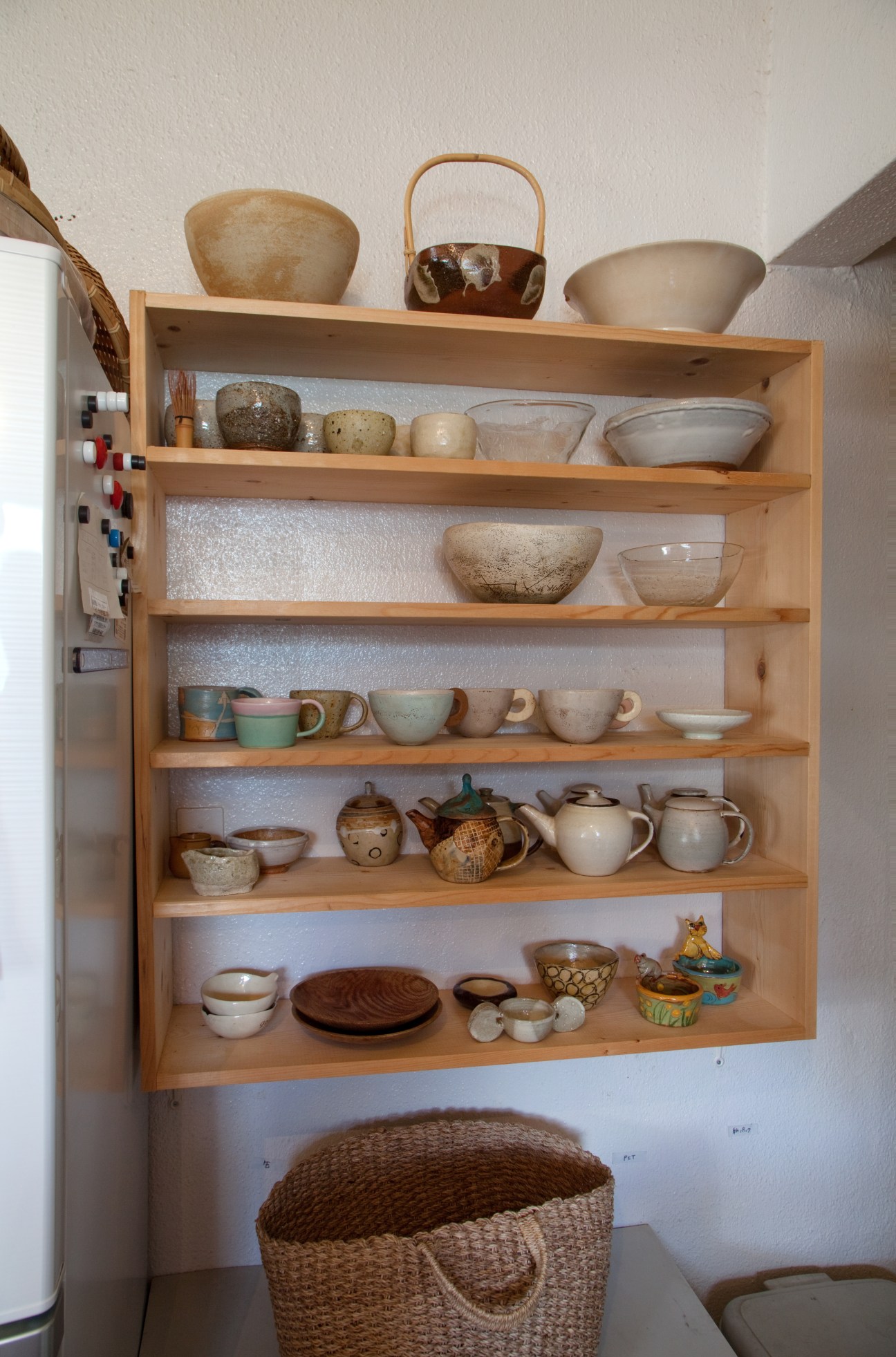 Wooden shelving unit displaying handmade ceramics, bowls, and textiles from Okinawa.