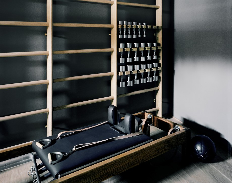 Ett Hem hotel basement gym with wooden shelving, chrome dumbbells, and exercise equipment against dark walls.