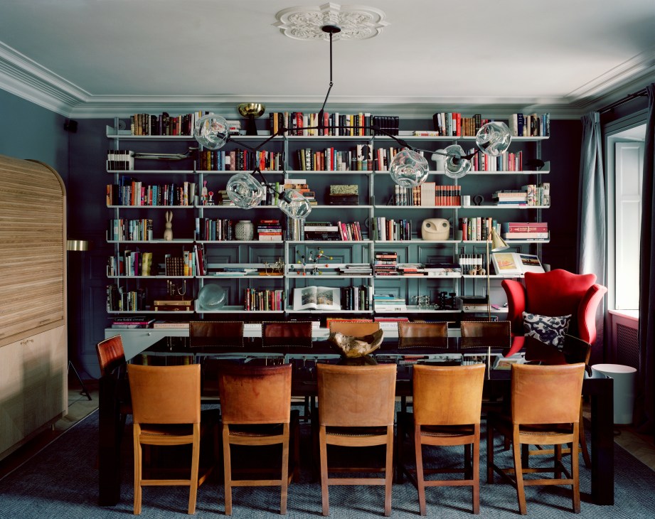 Library with floor-to-ceiling shelving filled with books and objects, dining table with tan leather chairs, and red armchair.