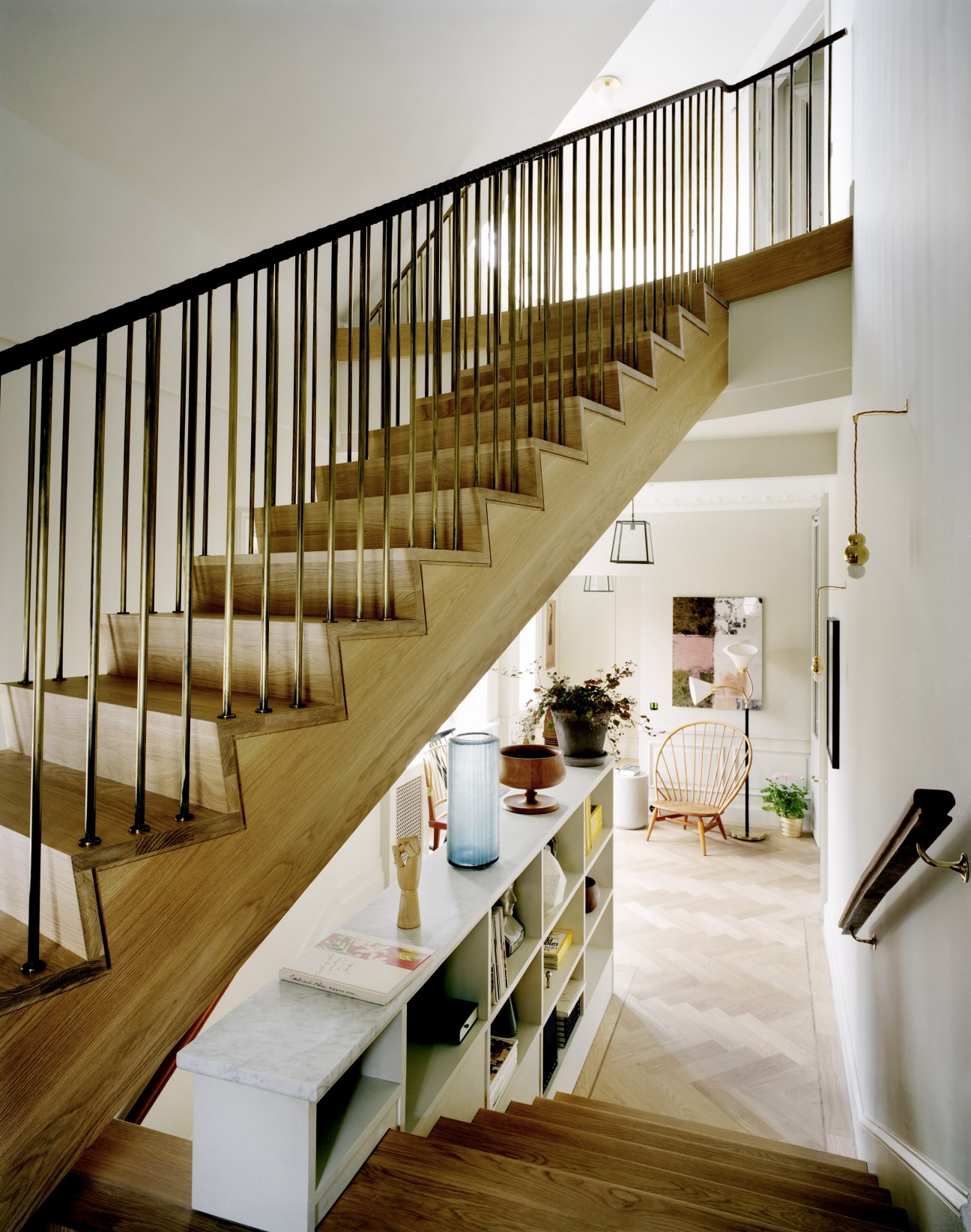 Modern wooden staircase with black metal railings and built-in reading nooks beneath, flooded with natural light from skylights above.