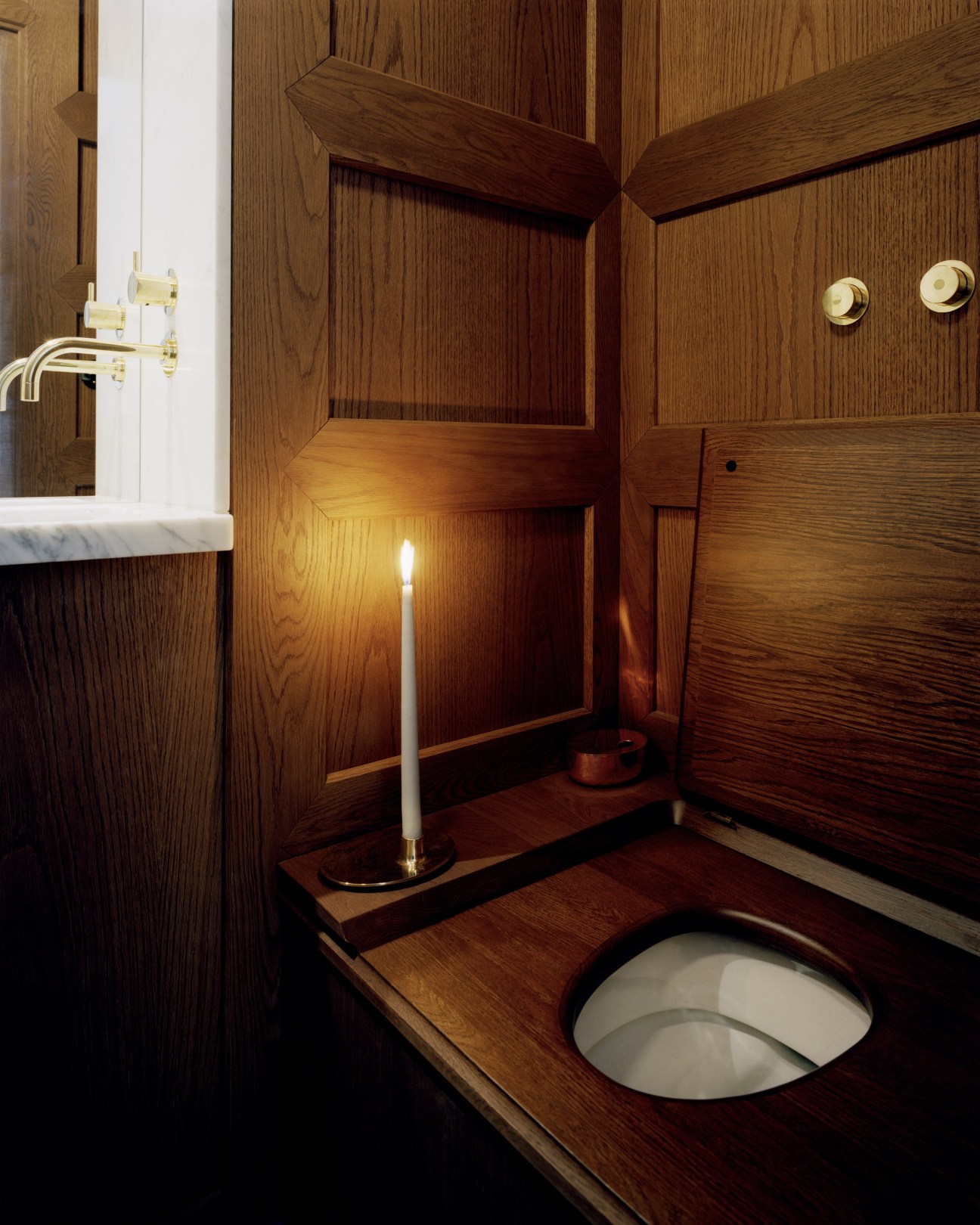 Wood-panelled bathroom with marble basin, brass fixtures, candle, and old-fashioned water closet at Ett Hem hotel.