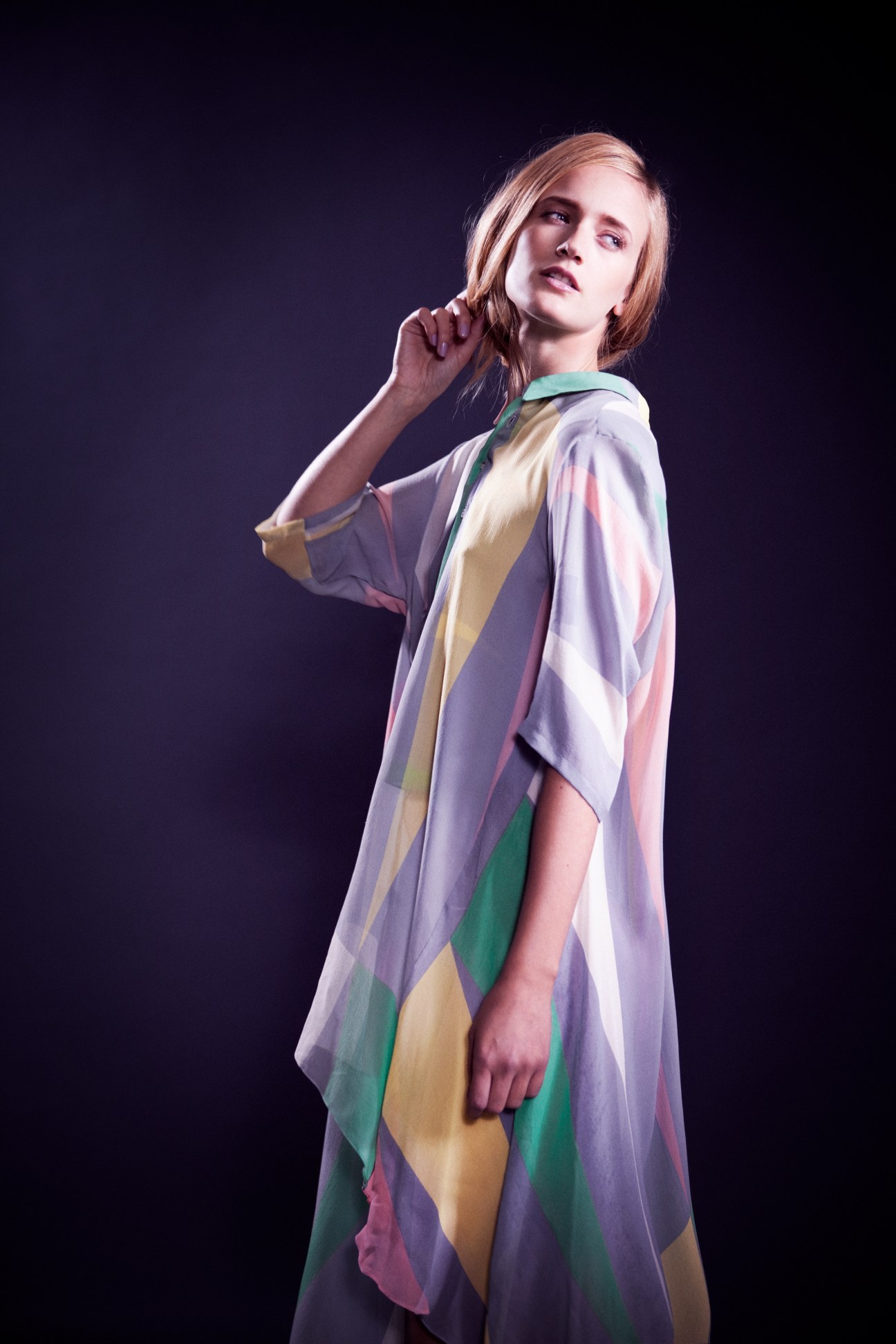 Woman wearing a colorful striped wrap dress with vertical bands of purple, cream, pink and green on a dark background.