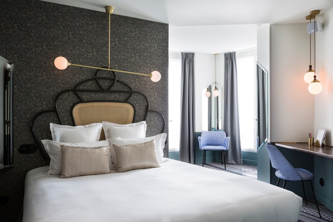 Hotel Panache Paris bedroom with dark patterned wallpaper, brass sconce lighting, and rattan headboard.