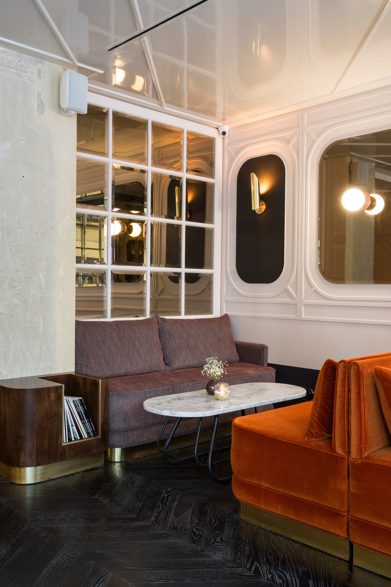 A modern hotel lounge with a grey sofa, orange armchair, marble table, and brass fixtures.