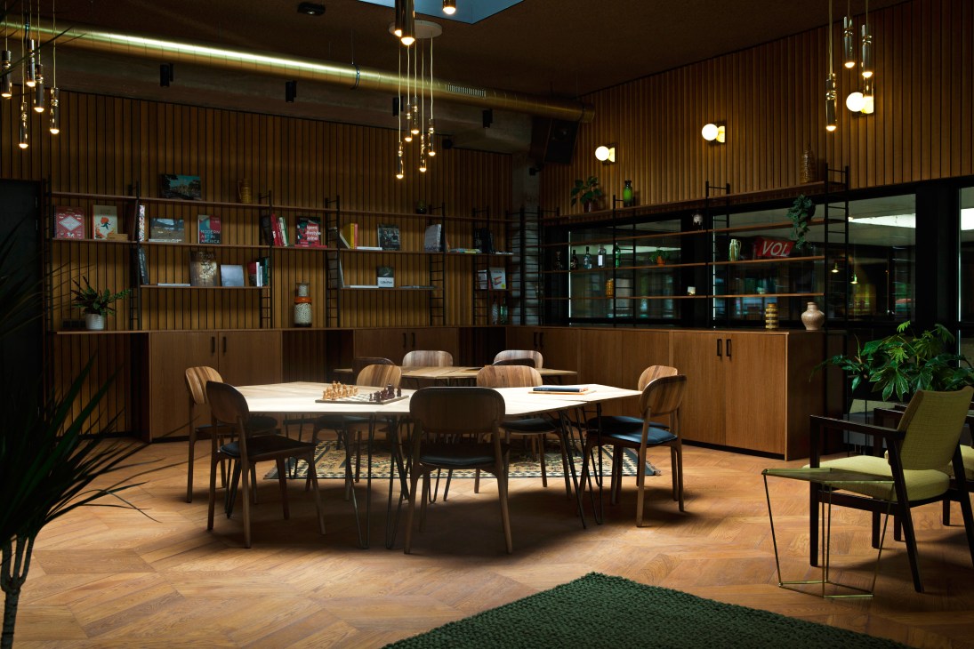 Modern hotel lounge with wooden walls, pendant lights, and contemporary furniture around a white table.