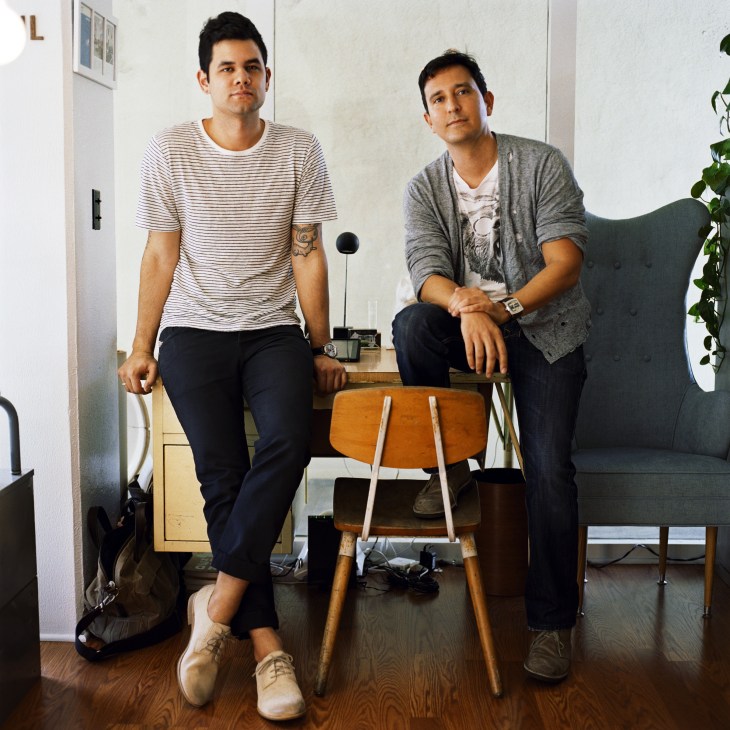 Two men sitting on mid-century chairs in a bright, minimal interior space at Hound & Quail, Honolulu.