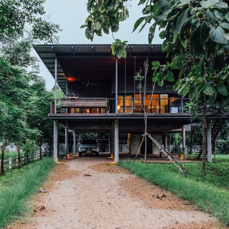 Modern elevated tropical house with timber and metal construction, surrounded by lush green vegetation.