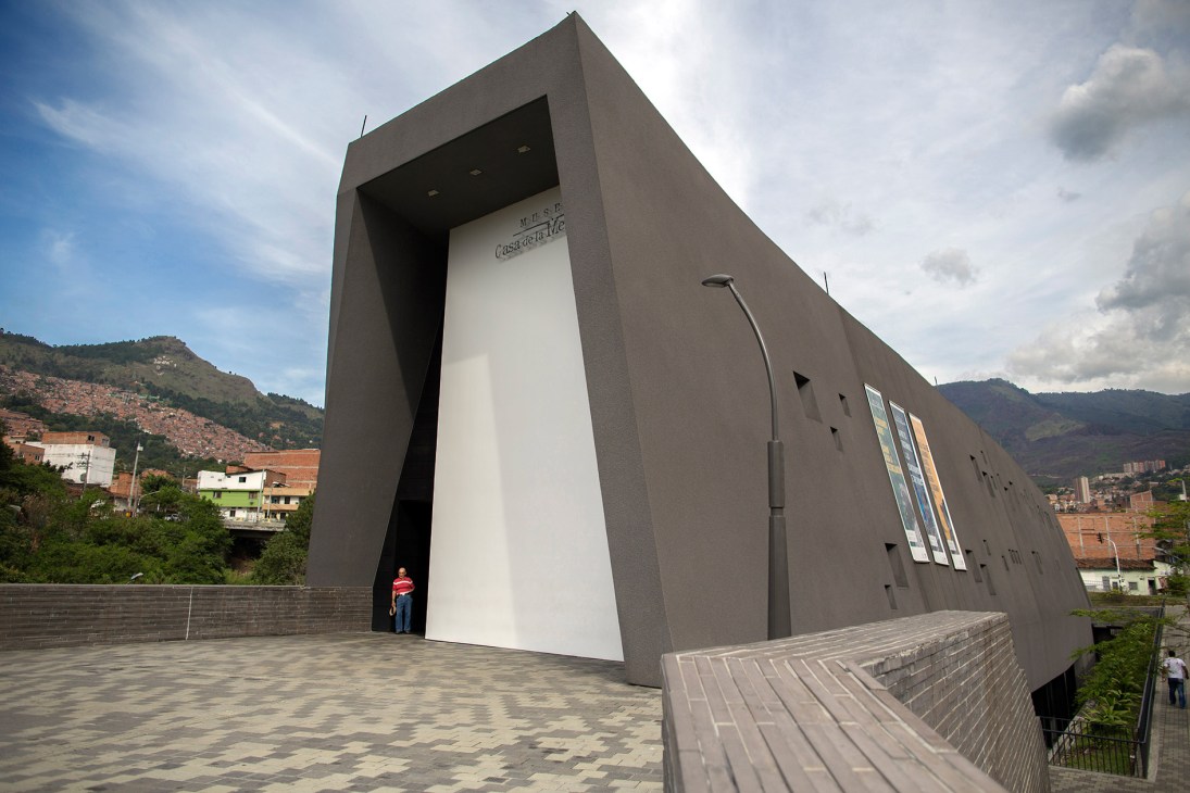 House of Memory museum exterior in Medellín with paved walkway and hillside slums in background.