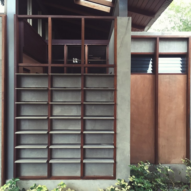 Wooden louvered window with horizontal slats in a dark red frame on a concrete wall.