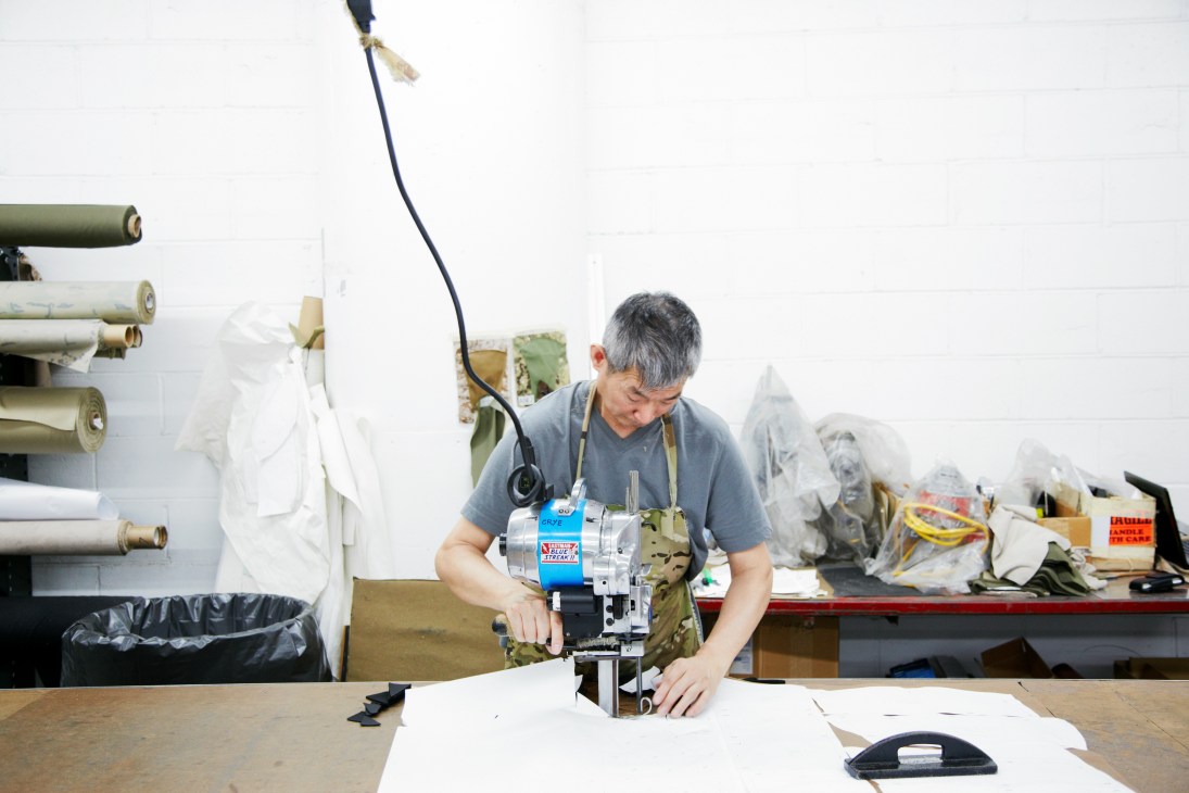 Worker hand-cutting camouflage fabric at Crye Precision manufacturing facility.
