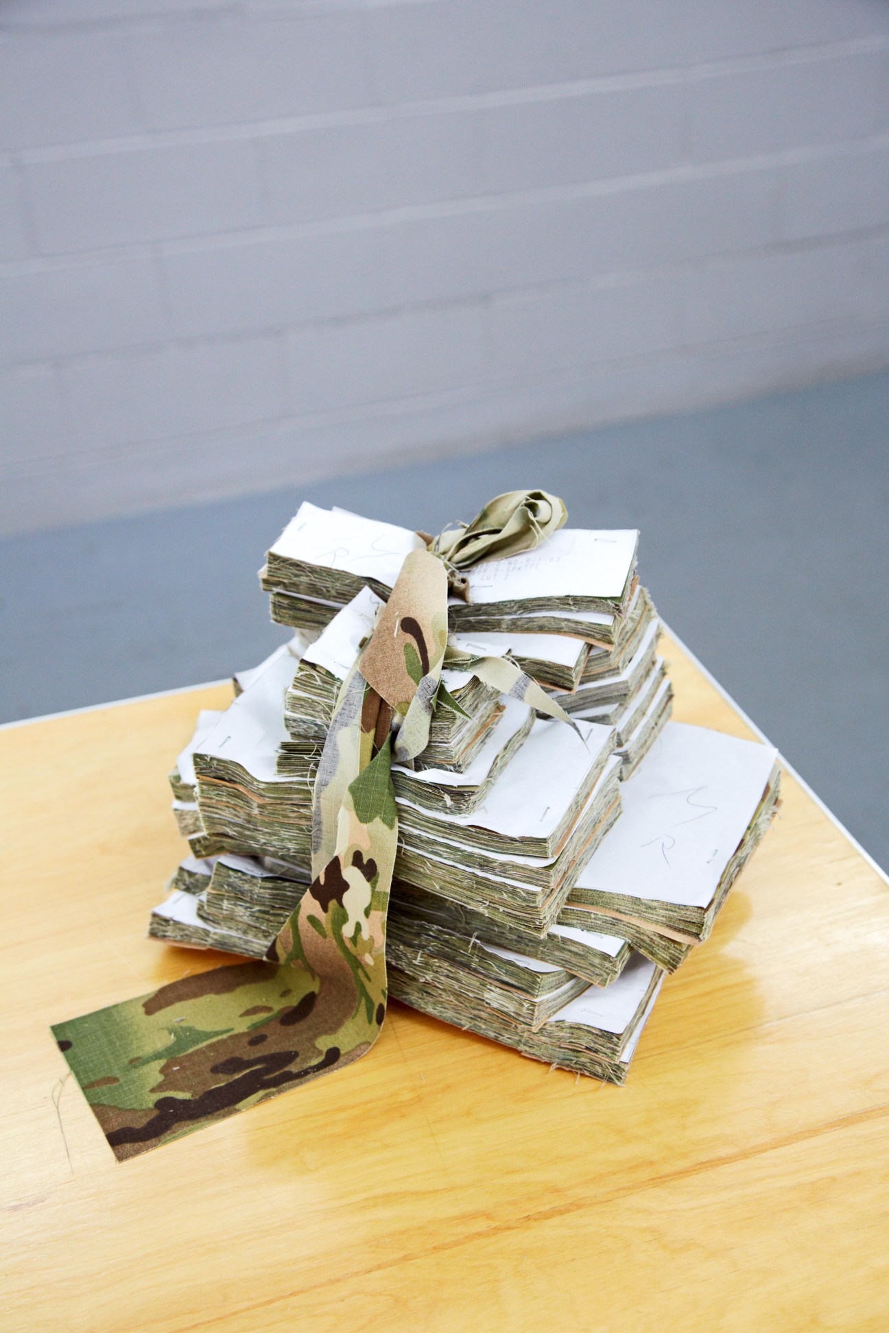 Stacks of paper samples tied with MultiCam camouflage patterned webbing on a wooden surface.
