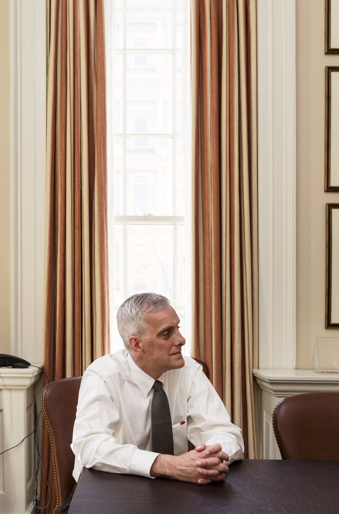 Denis McDonough in an office, seated at a desk wearing a white shirt and tie.