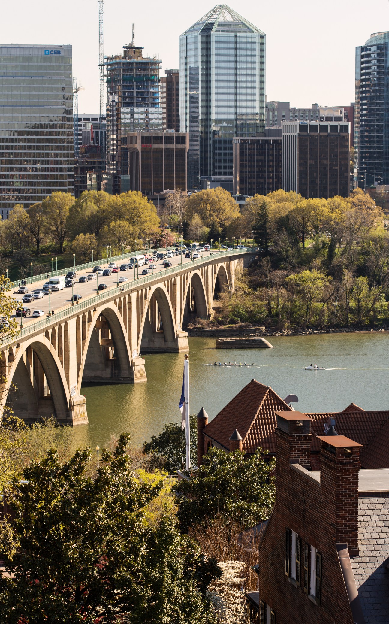 View of Washington D.C. skyline from Georgetown University, showing an arched stone bridge over the Potomac River with spring foliage.