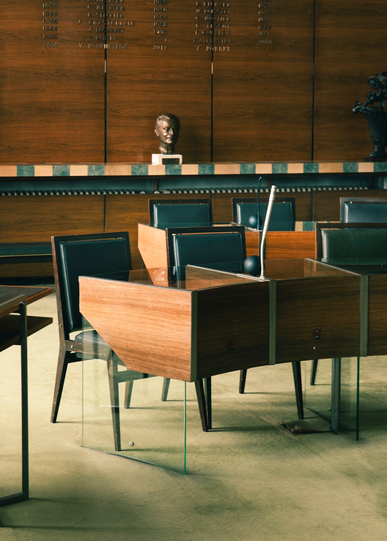 Council chamber with wooden furniture, dark leather chairs, and a bust on wood-paneled wall