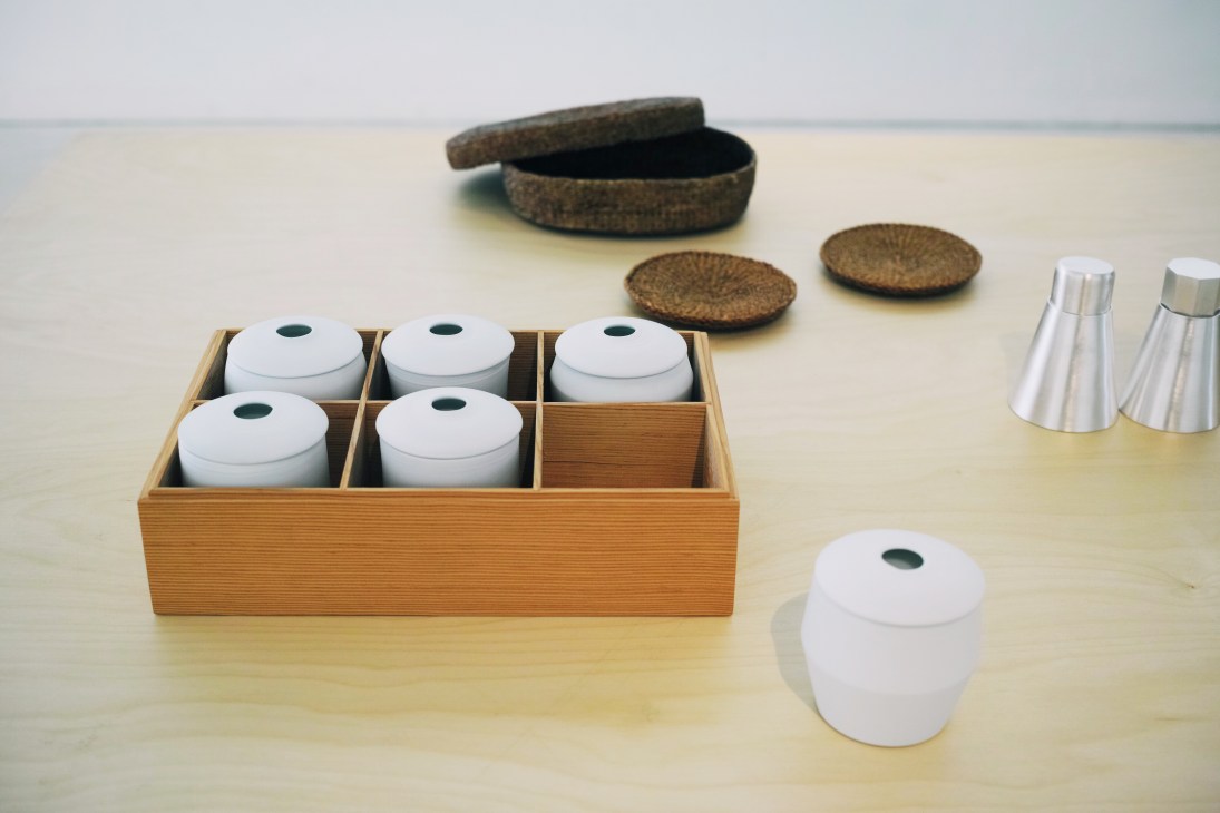 White porcelain lidded bowls by Ko Hee Sook displayed with wooden box, woven coasters and metal vessels.