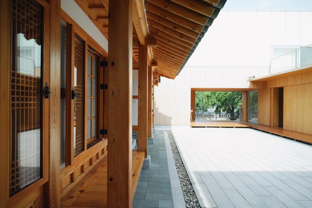 Traditional Korean hanok house with wooden latticed doors and beams overlooking a stone-paved courtyard.