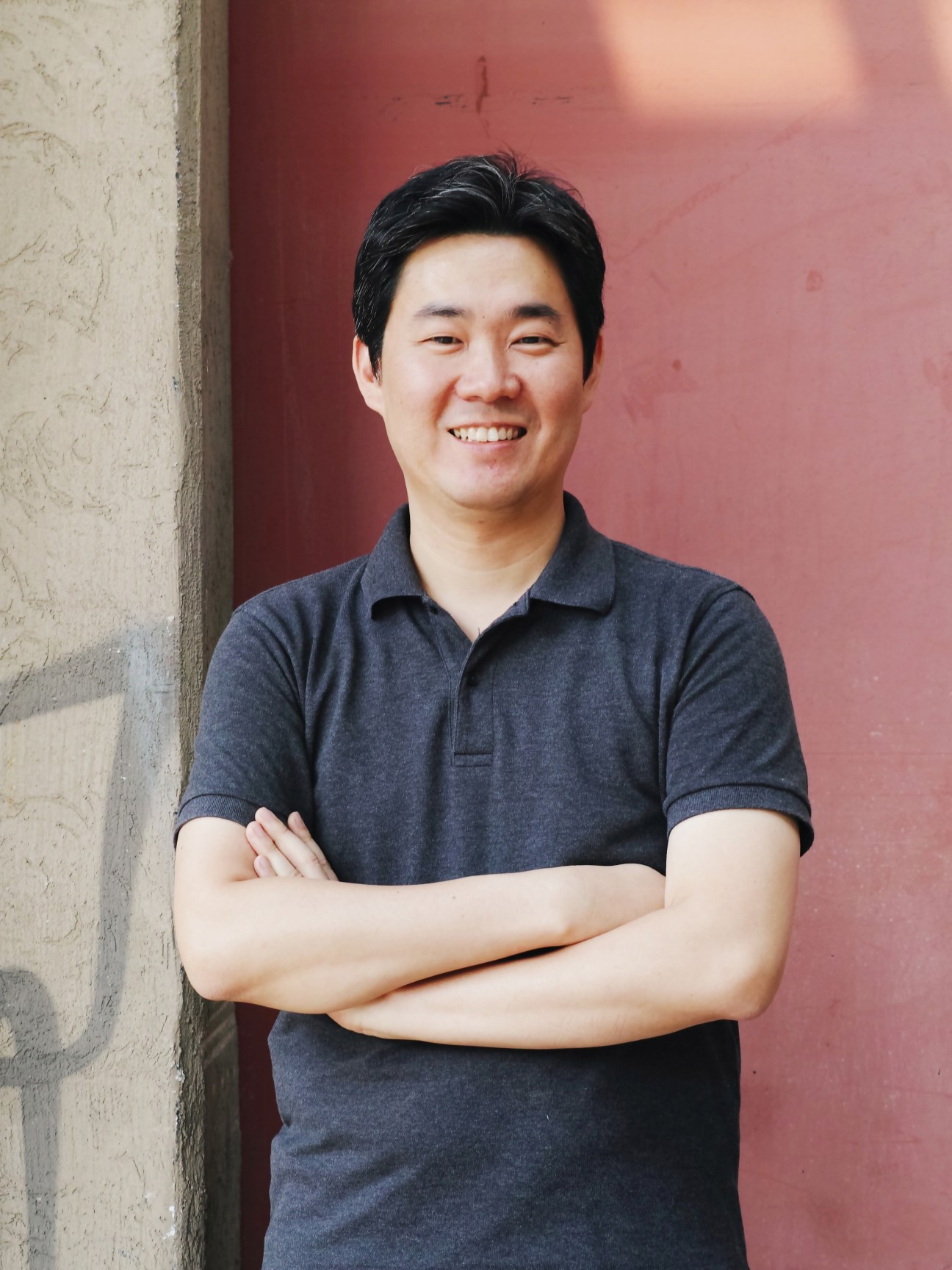 Designer Jihoon Ha smiling at camera against a red and white wall background.