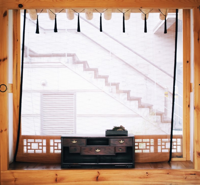 Antique dark wooden chest displayed in a traditional Korean hanok room with wooden beams and latticed windows.