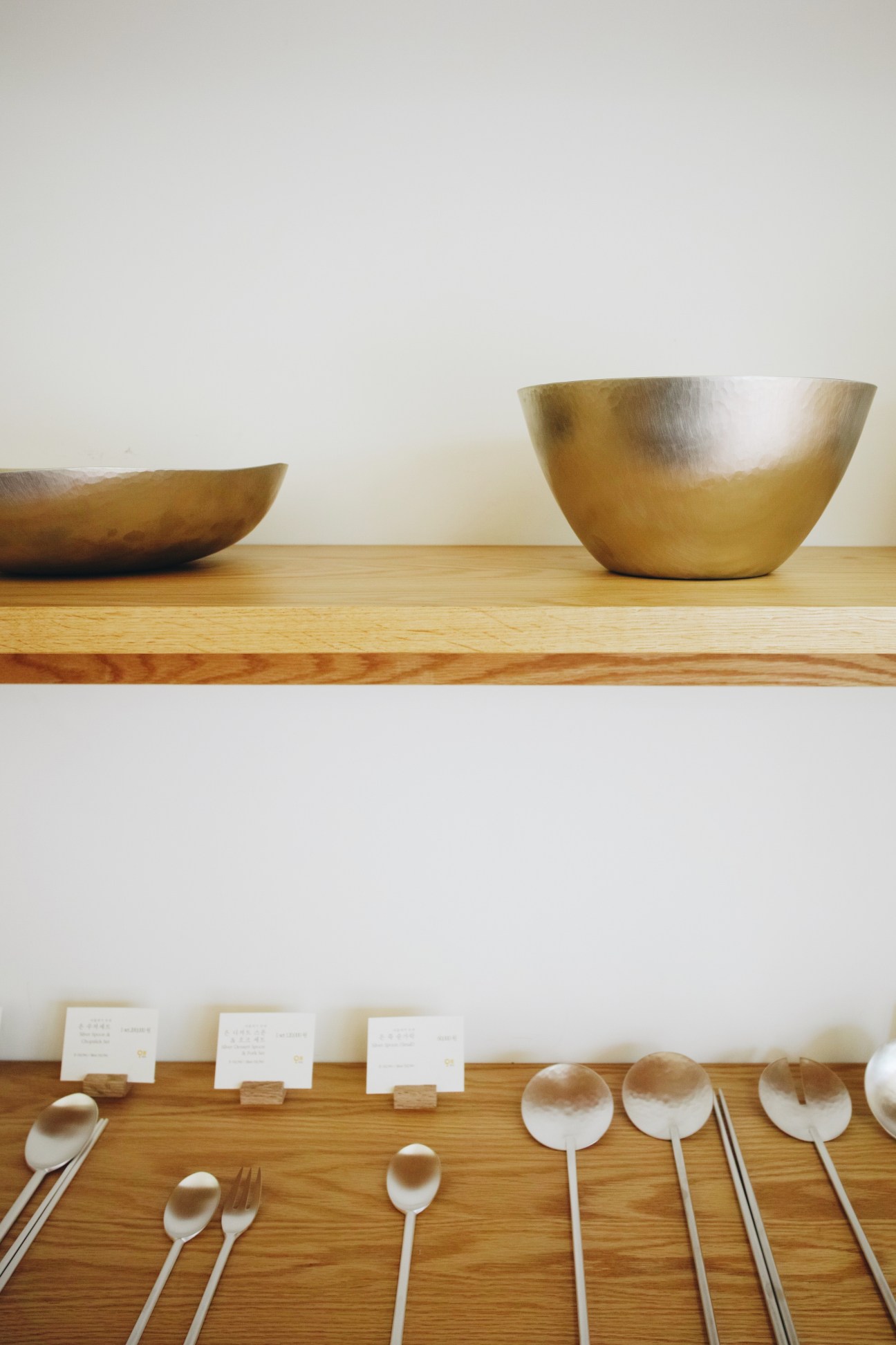 Minimalist display of brass bowls and white spoons arranged on wooden shelves in the Arumjigi Foundation shop.