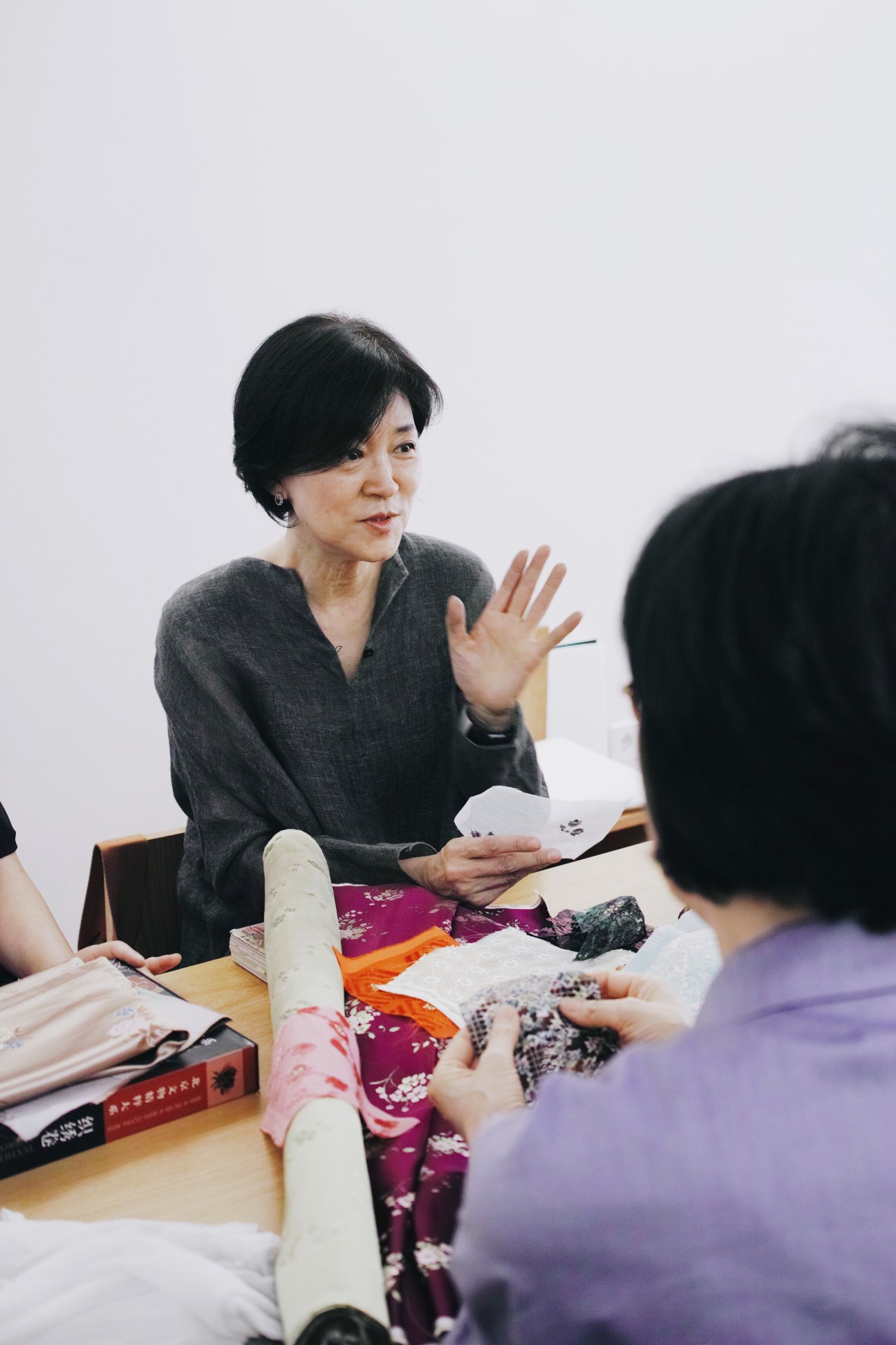 Yun Gyun S Hong, chairwoman of the Arumjigi Foundation, gestures while discussing fabric samples at a wooden table.