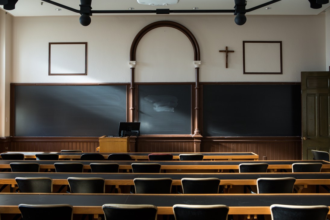 Empty Georgetown classroom with wooden seats, blackboards, and a wooden crucifix on the wall reflecting Jesuit heritage.