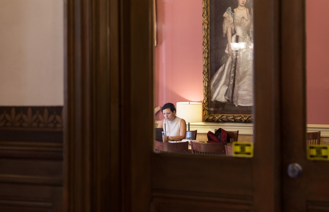 Student studying at a desk in a library study room with framed portrait on wall.