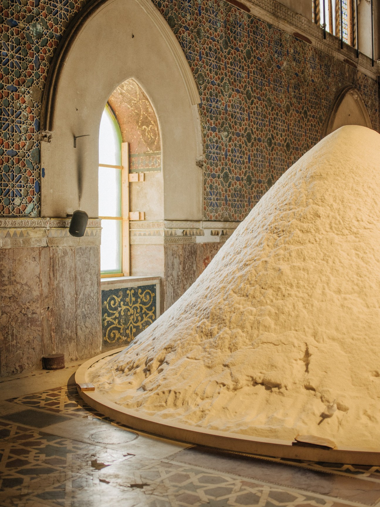 Large mound of salt displayed inside an ornate palazzo with patterned walls and arched window.