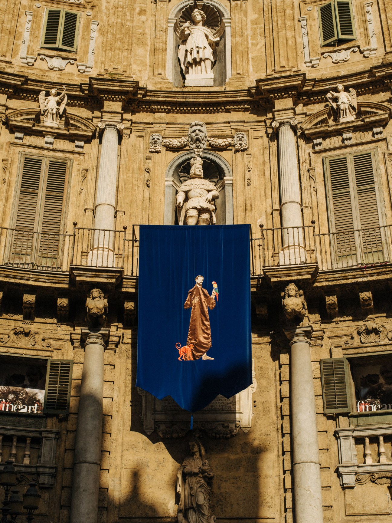 Blue tapestry with gold figure and dog hanging on ornate palazzo facade at Quattro Canti