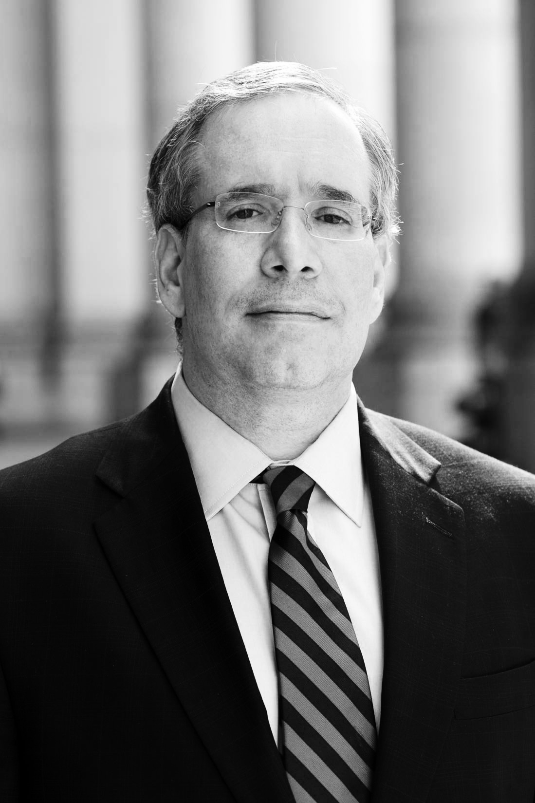 Black and white portrait of Scott Stringer, Manhattan Borough president, wearing glasses and a striped tie.