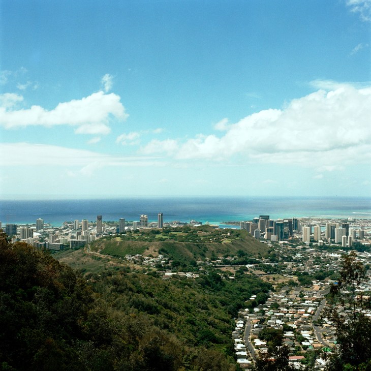 Aerial view of Honolulu cityscape with high-rise buildings, beaches, and green volcanic crater surrounded by ocean.
