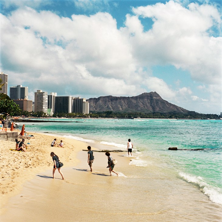 Waikiki beach with swimmers and surfers in turquoise water, high-rise hotels, and Diamond Head mountain in the background.