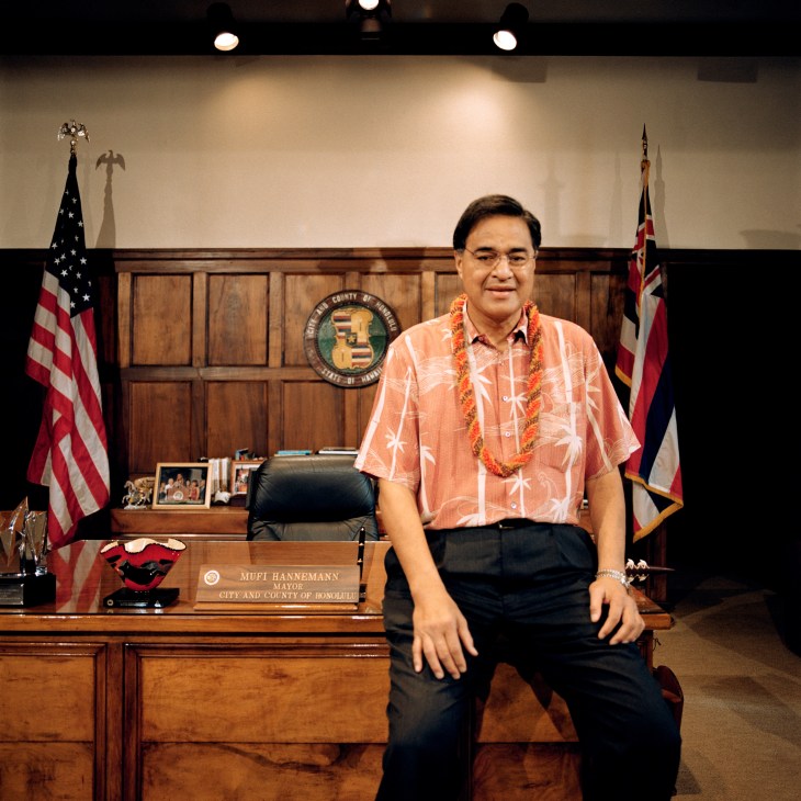 Mayor Mufi Hannemann sits at his desk wearing a coral Hawaiian shirt and lei garland in his Honolulu office.