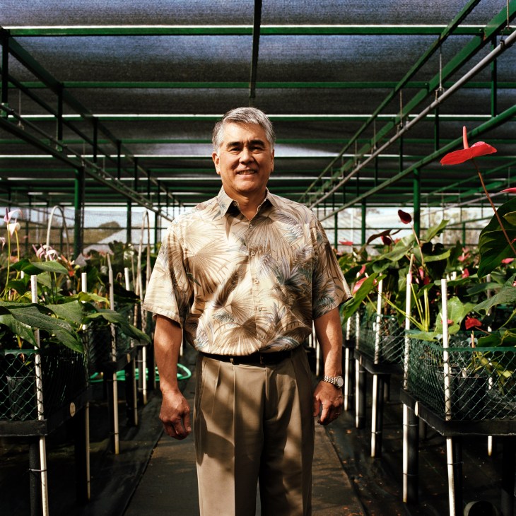 Andrew Hashimoto, dean of the College of Tropical Agriculture at University of Hawaii, stands in a greenhouse among tropical flowering plants.