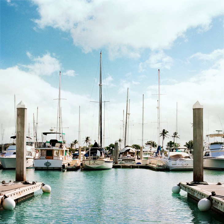 Sailboats and yachts moored at Ko Olina resort and marina with turquoise water and wooden dock posts.