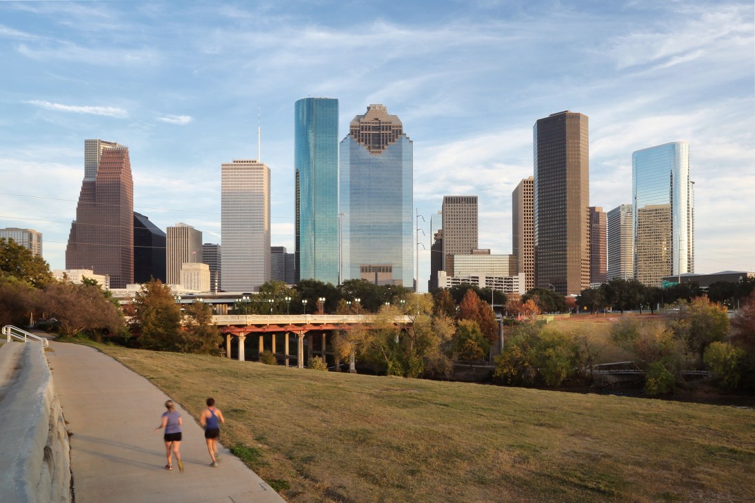 Houston's downtown skyline with modern skyscrapers viewed from a green park with runners on a path.