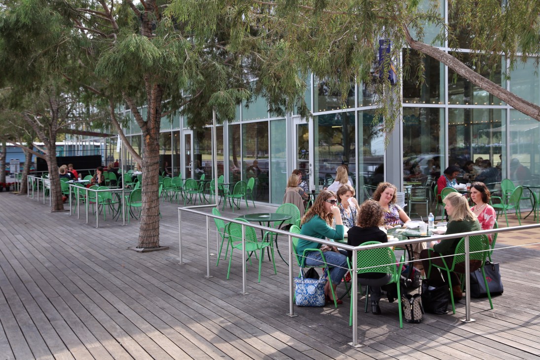 Outdoor seating area at Lake House Café with green chairs and tables under large trees.