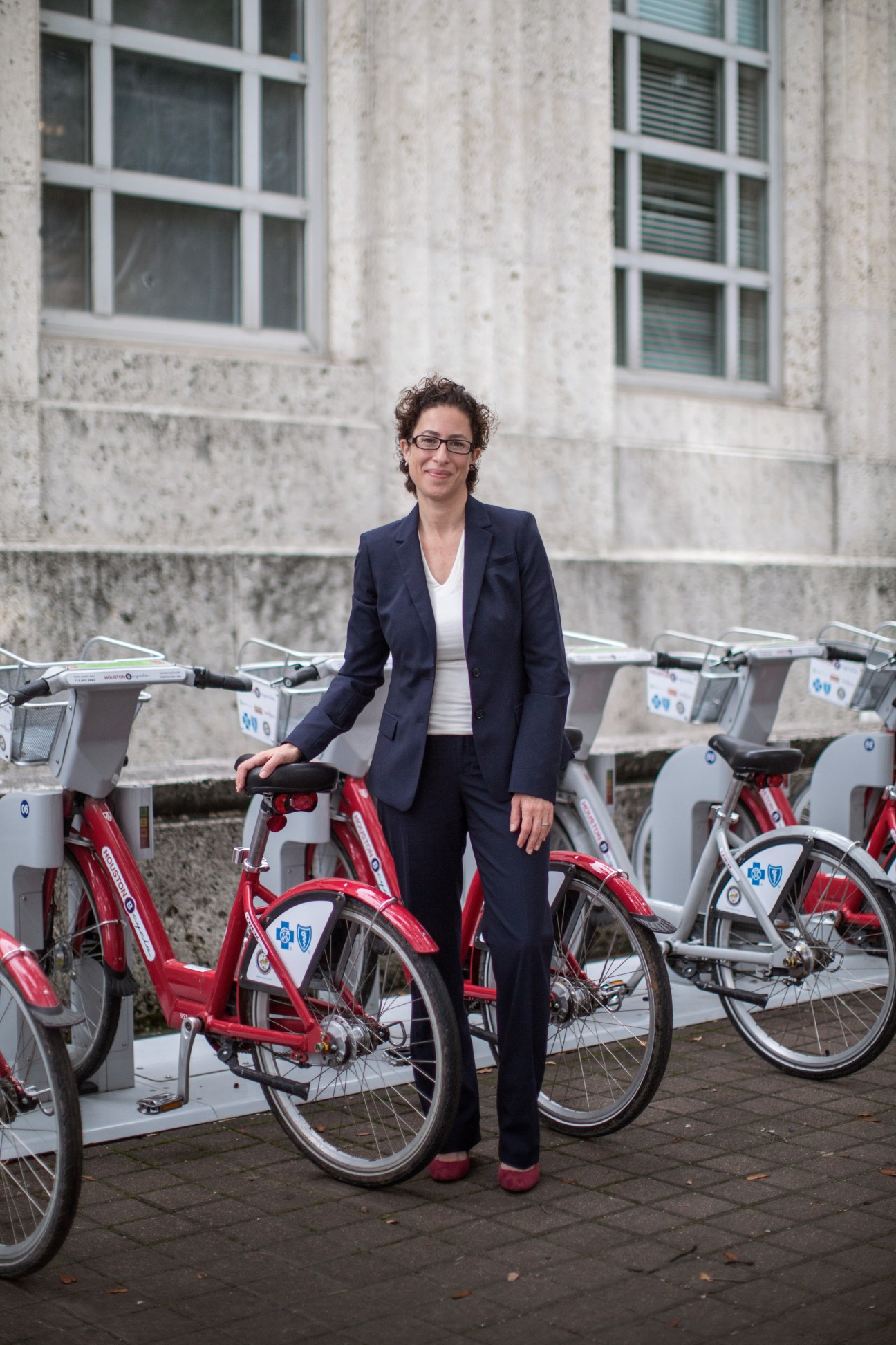 Houston sustainability director Laura Spanjian poses with shared red bicycles against a concrete building.