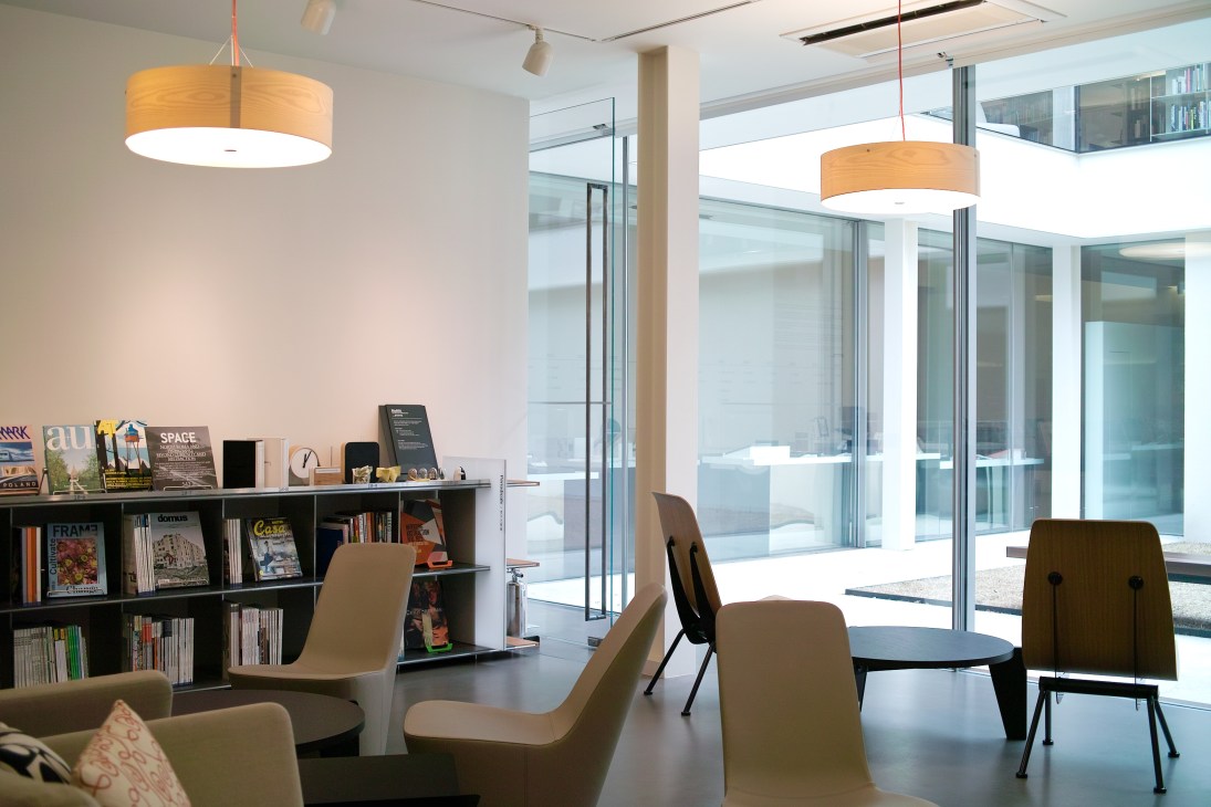 Modern café interior with bookshelves, pendant lighting, and floor-to-ceiling windows overlooking a courtyard.