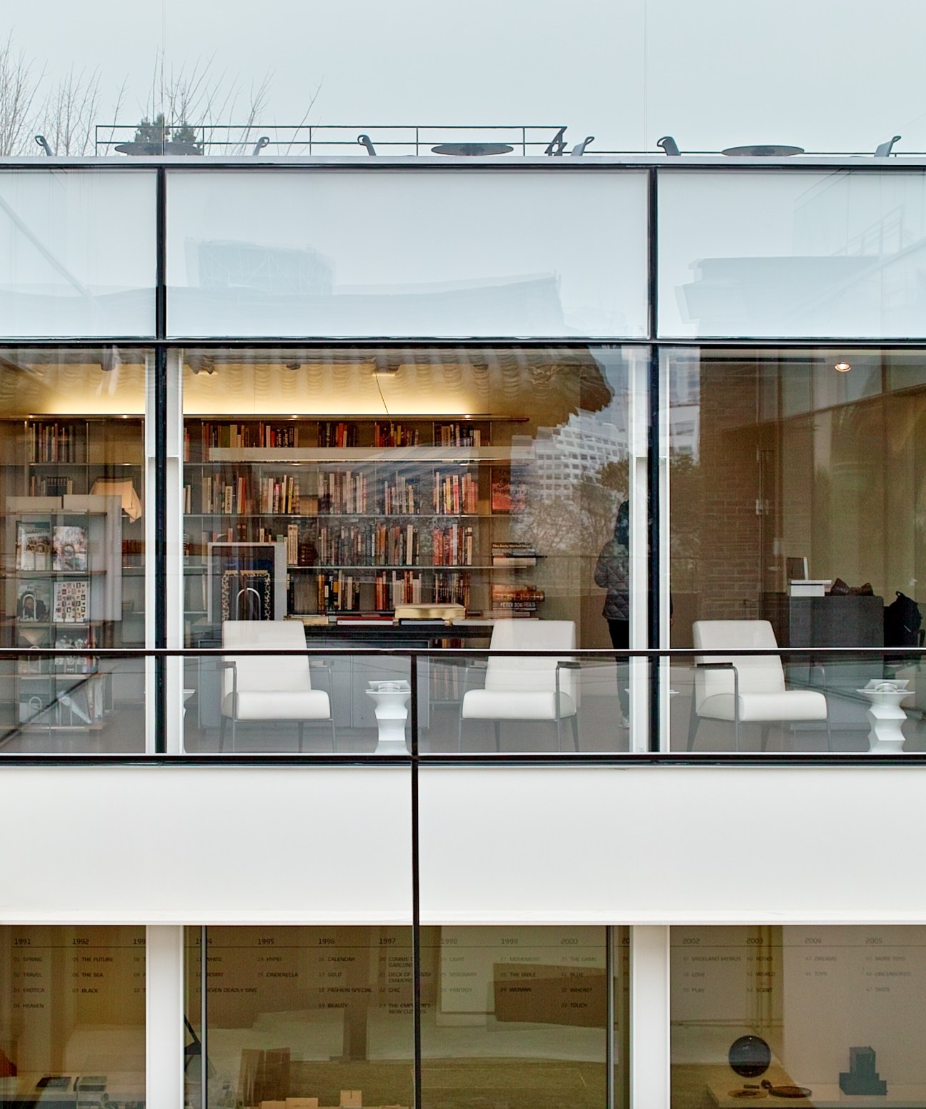 Small reading room with white chairs and bookshelves visible through large windows at Hyundai Card Design Library.