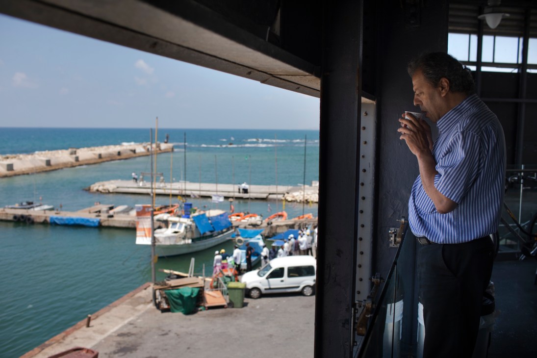 Man in blue striped shirt holds coffee cup while looking out over Jaffa port from i24 News studios