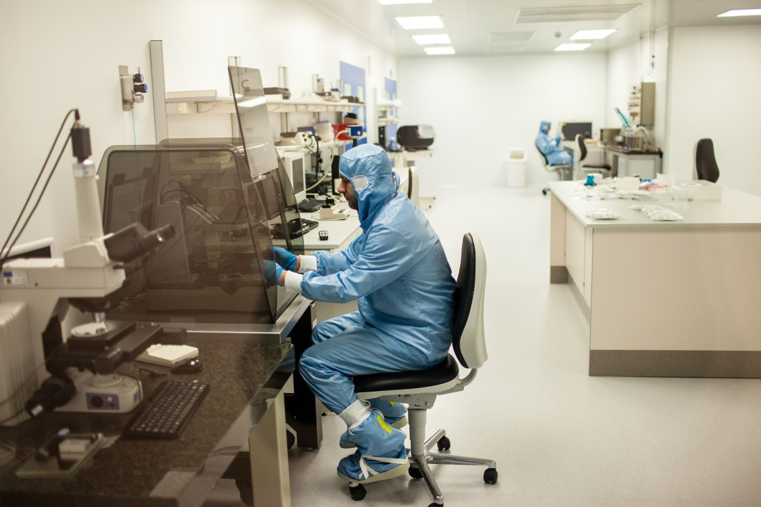 Laboratory technician in blue cleanroom suit working at equipment in a modern research facility.