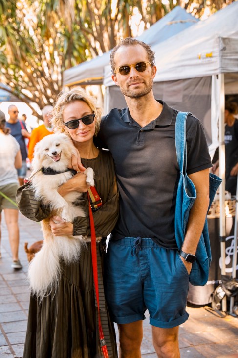 Couple with dog enjoying Kings Cross Market under palm trees and market tents.