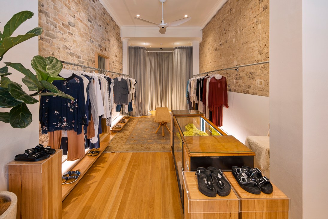 Interior of Byfreer boutique showing minimalist womenswear displayed on racks with exposed brick walls and wooden flooring.
