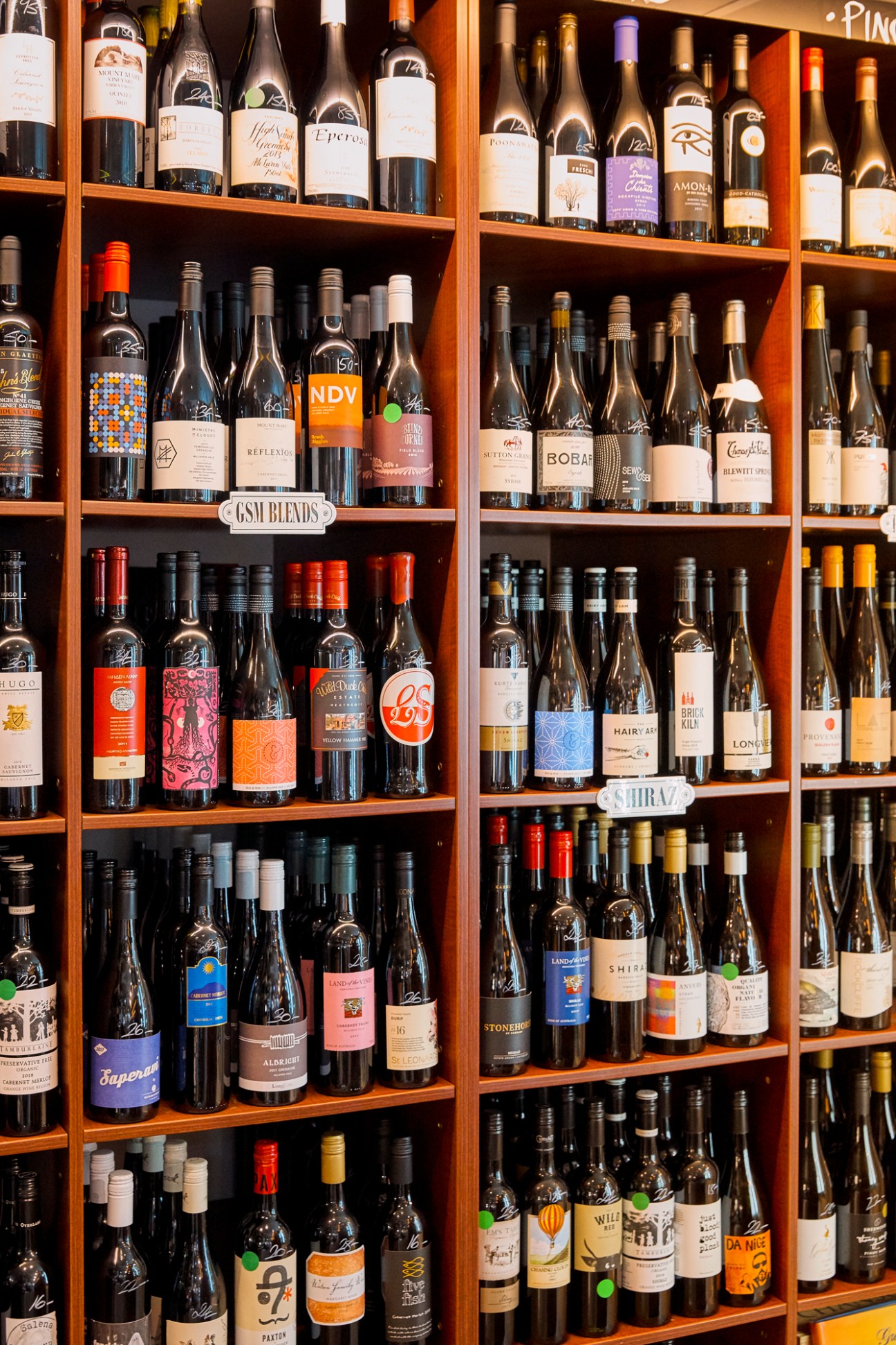Wooden shelves stocked with wine bottles organized by varietal at Bottega del Vino.