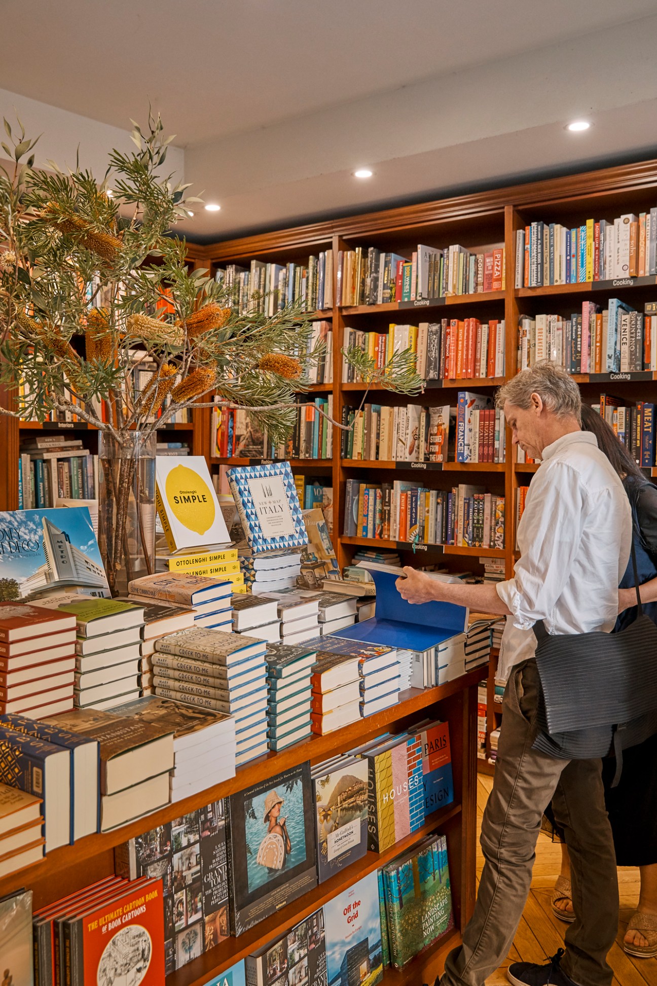 Customer browsing books at Potts Point Bookshop with wooden shelves and display table.