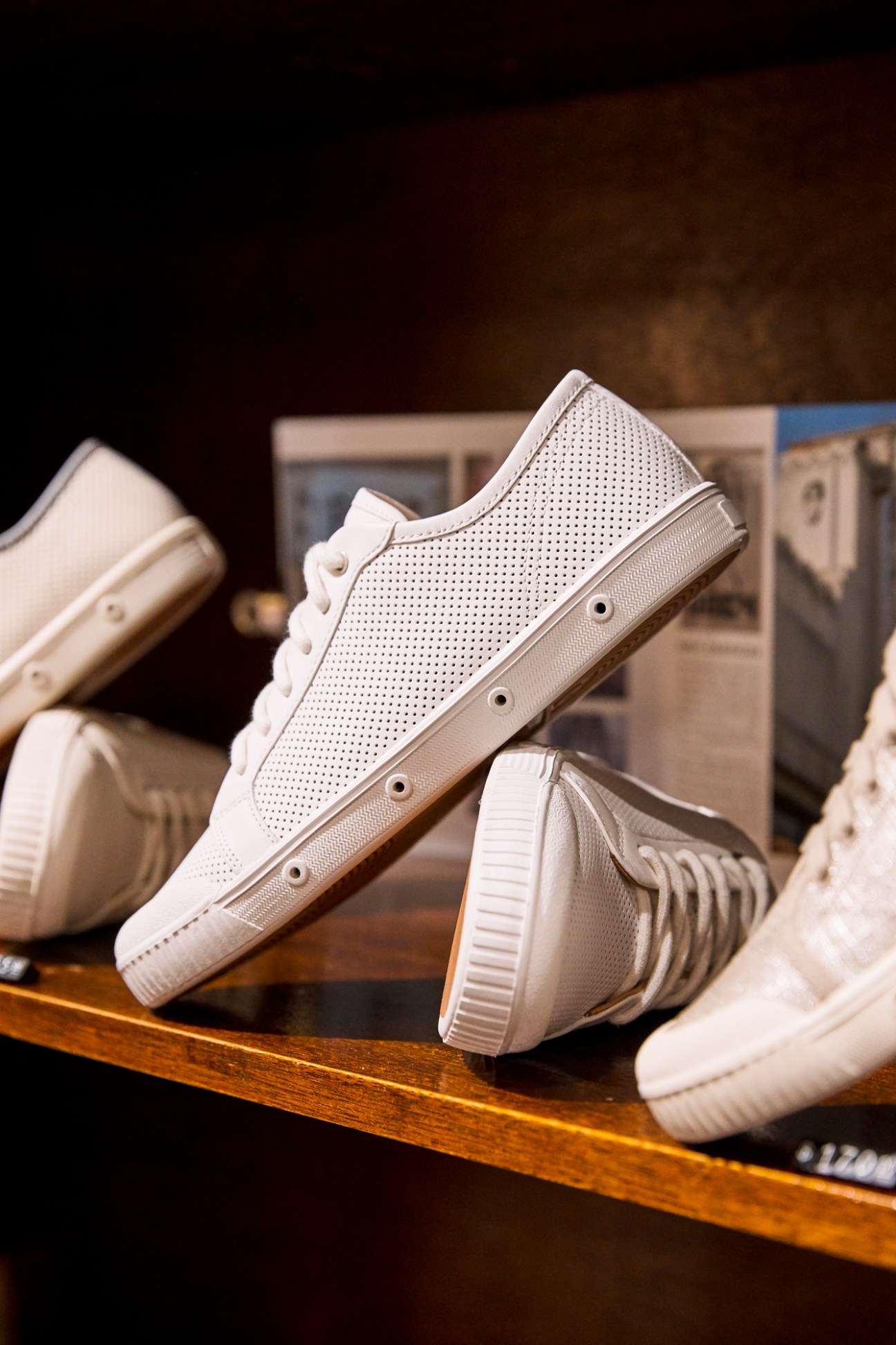 White perforated leather trainers displayed on a wooden shelf in Spring Court store.