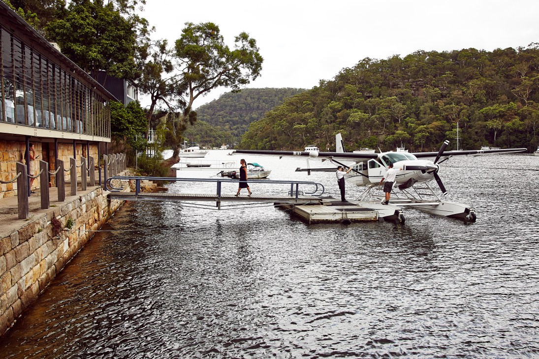 Chef plating dishes at Berowra Waters Inn with seaplanes and river in background.